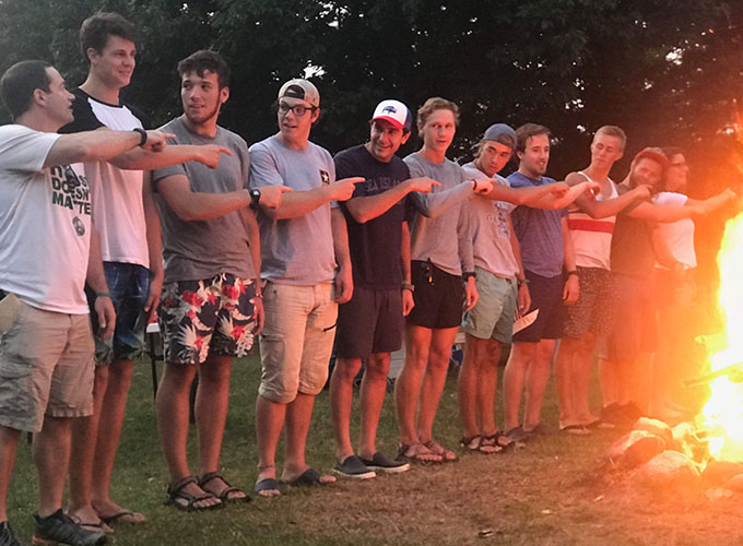 A group of counselors and staff members at North Star Camp for Boys participate in a campfire activity in which they each point to the person on their left.