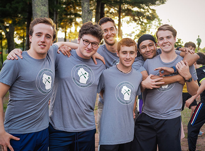 Staff members and campers at North Star Camp for Boys smile with their arms around each other wearing matching t-shirts.