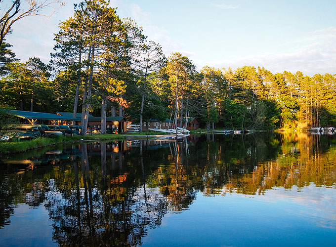 Scenic picture of trees reflecting the lake and boats parked near the shoreline at North Star Camp for Boys.