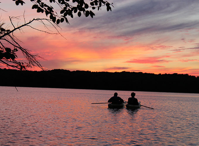 Two North Star Camp for Boys campers float down Spider Lake in canoes at sunset.