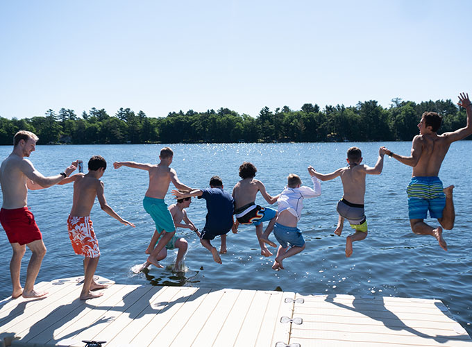 A group of North Star Camp for Boys campers hold hands while jumping off the dock into Spider Lake.