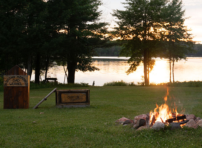 A campfire burns with the lake in the distance.