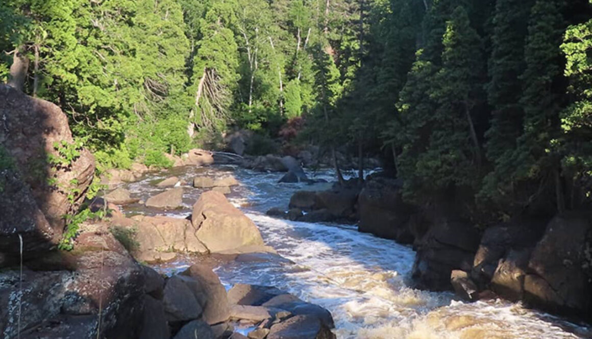 River flowing near rocks and surrounding trees, a scenic view of one of the hiking trips at North Star Camp for Boys.