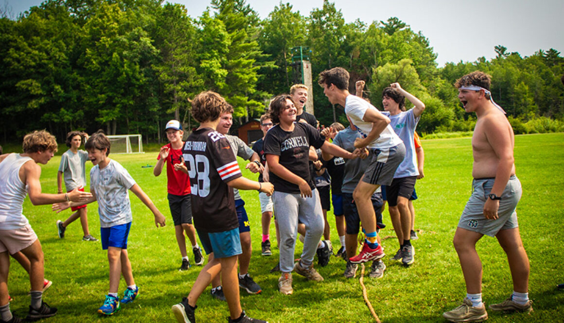 A group of campers jump, smile, cheer, and high-five around a rope, after winning a game of tug-of-war at North Star Camp for Boys.