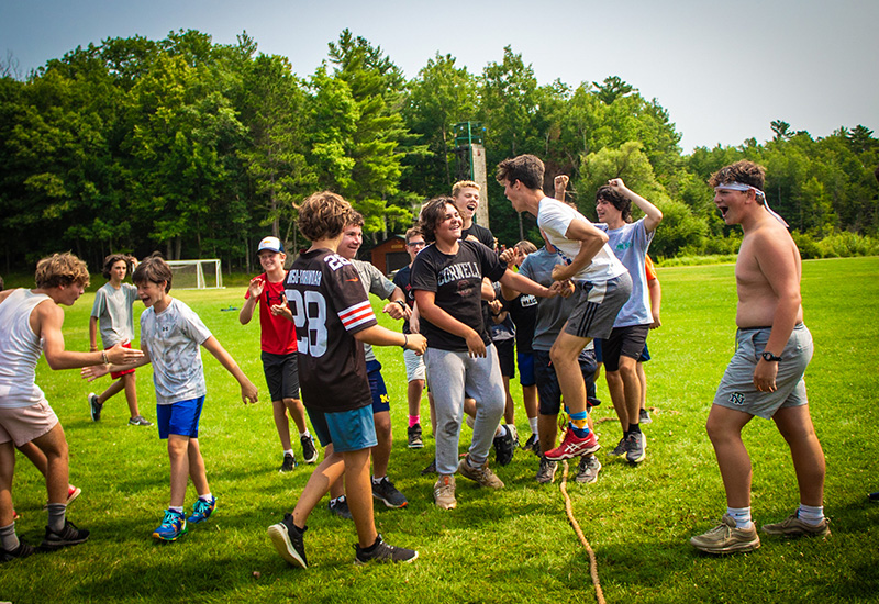 A group of campers jump, smile, cheer, and high-five around a rope, after winning a game of tug-of-war at North Star Camp for Boys.