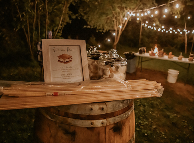 Marshmallows in glass jars are set on a table with a picture frame holding a smore's menu at an outdoor wedding at the North Star Camp for Boys facility.