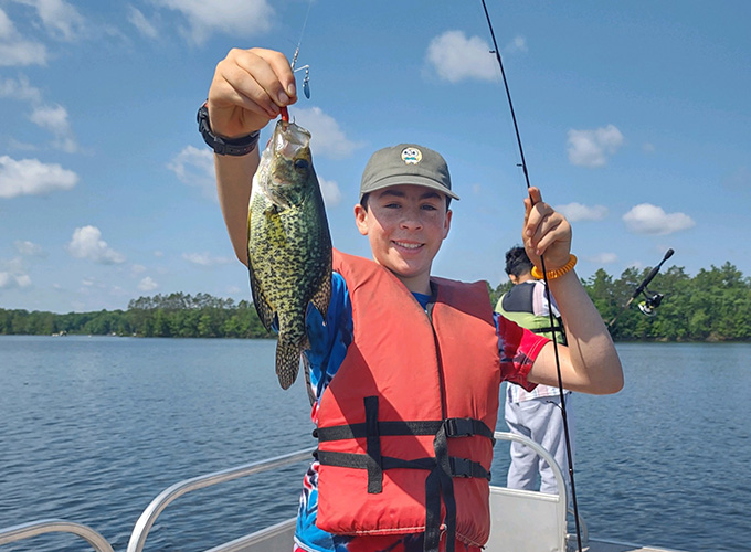 A camper poses while holding a fish he just caught at North Star Camp for Boys.