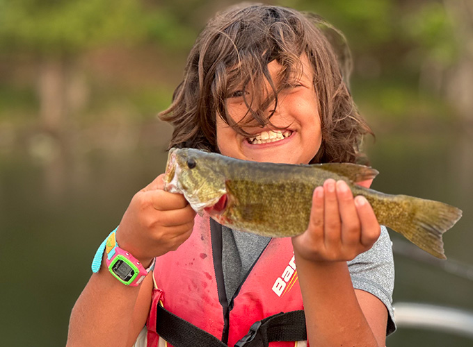 A camper poses while holding a fish he just caught at North Star Camp for Boys.