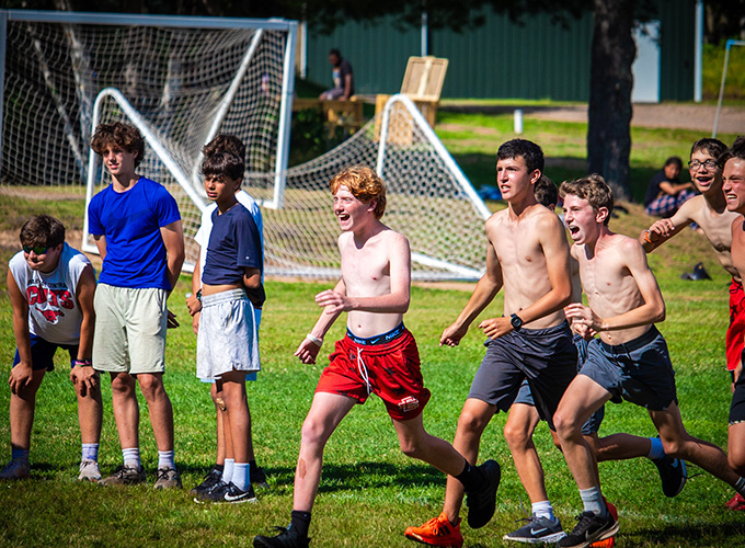 A group of campers run in a line on a soccer field while participating in the college days competition at North Star Camp for Boys.