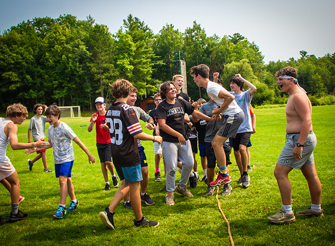 A group of campers at North Star Camp for Boys smile and celebrate around a tug of war rope during the college days competition.