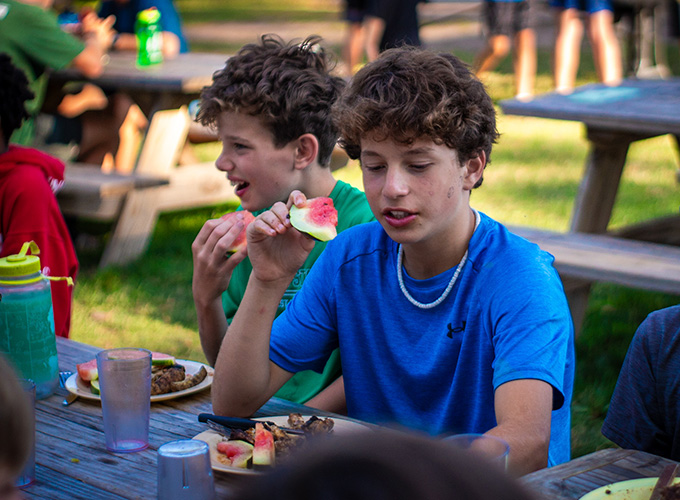 Campers laugh while eating watermelon at mealtime at North Star Camp for Boys.