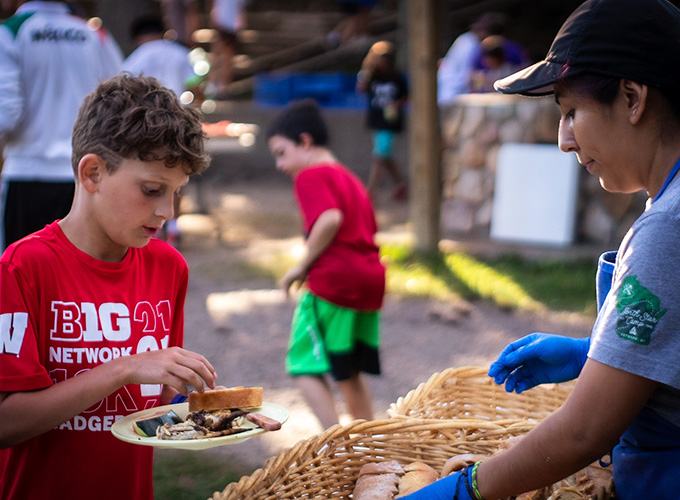 A camper adds a piece of bread to his plate as he goes through the food line during mealtime at North Star Camp for Boys.