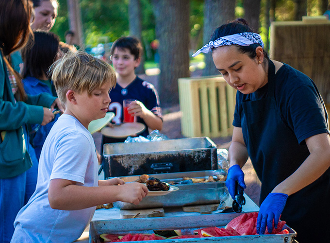 A kitchen staff member serves a camper a slice of watermelon at the buffet during mealtime at North Star Camp for Boys.