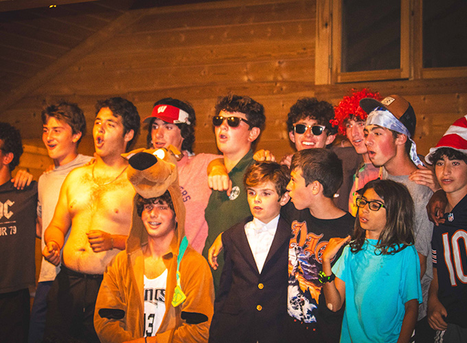 A group of campers wearing various costumes including a Scooby Doo onesie, an oversized suit, and sunglasses participate in a theater play at North Star Camp for Boys.