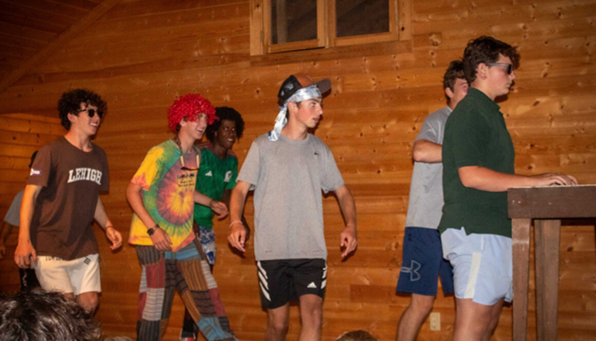 Campers at North Star Camp for Boys stand on stage in a log cabin while participating in a theatrical performance.