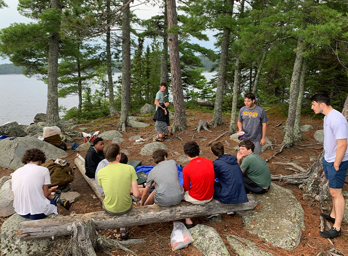 A group of campers sit on a log in the forest of Quetico Provincial Park in Ontario, Canada during "The Canadian" wilderness trip at North Star Camp for Boys.