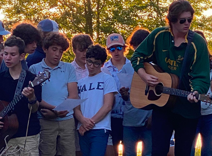 A group of campers gather around to sing a song while staff members play the guitar during a Friday Night Service at North Star Camp for Boys.