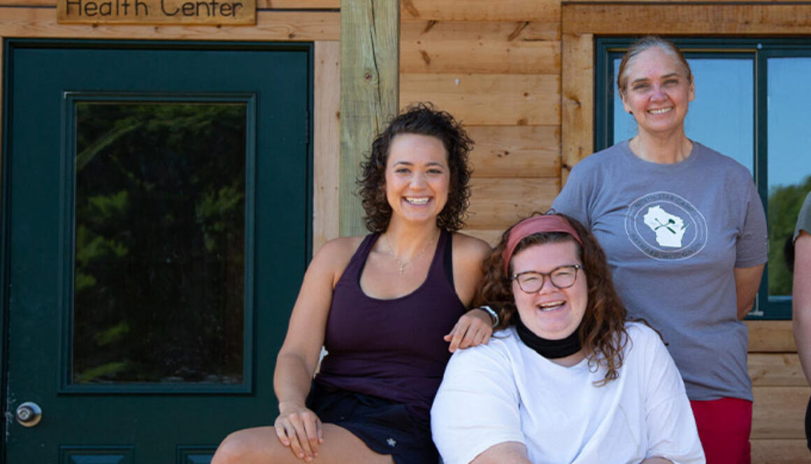 Three health staff members smile while sitting outside of the Handler Health Center at North Star Camp for Boys.