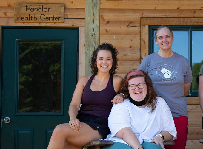 Three health staff members smile while sitting outside of the Handler Health Center at North Star Camp for Boys.