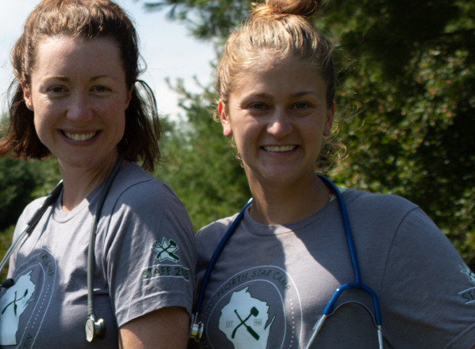 Two staff members wearing matching North Star Camp for Boys grey t-shirts smile with stethoscopes draped around their necks.