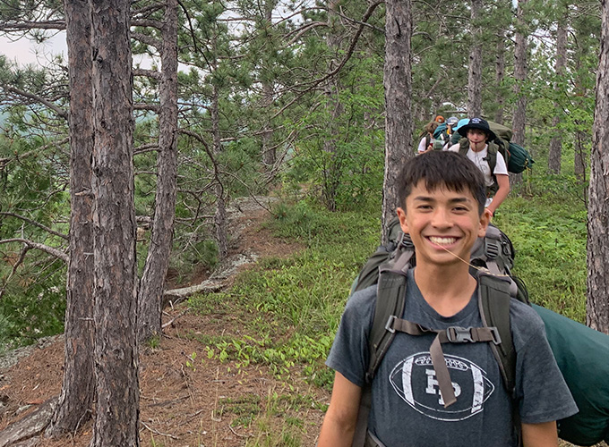 Campers wearing backpacks walk in a single file line through a hiking trail on a North Star Camp for Boys wilderness trip.