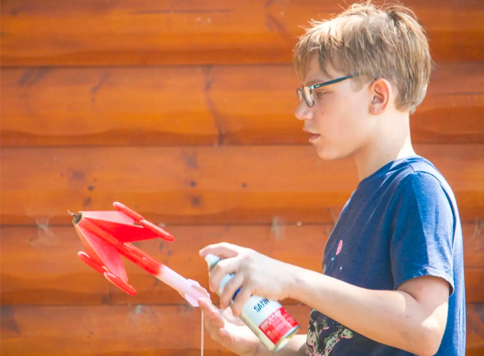 A camper uses red spray-paint to paint a rocket during a rocketry activity at North Star Camp for Boys.