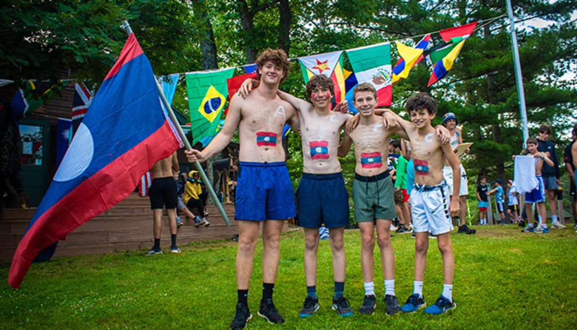 A group of campers wearing body paint to resemble the flag of Laos smile while standing in front of other international flags during United Nations Day at North Star Camp for Boys.