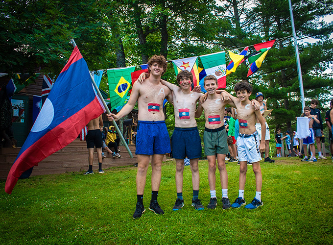 A group of campers wearing body paint to resemble the flag of Laos smile while standing in front of other international flags during United Nations Day at North Star Camp for Boys.