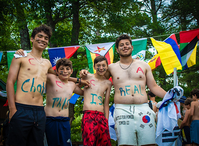A group of boys wearing body paint stand in front of international flags during United Nations Day at North Star Camp for Boys.
