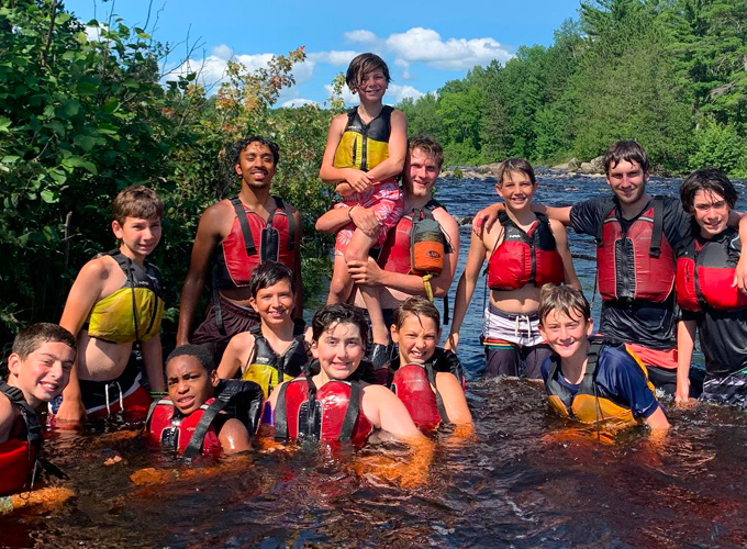 Campers and trip leaders wear life jackets and smile while swimming in the Flambeau River during a wilderness trip at North Star Camp for Boys.
