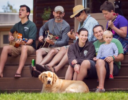 A group of Family Campers play music and sing songs on the office porch.