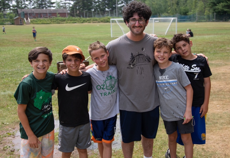 A North Star Camp counselor smiles with a group of campers on a warm summer day.