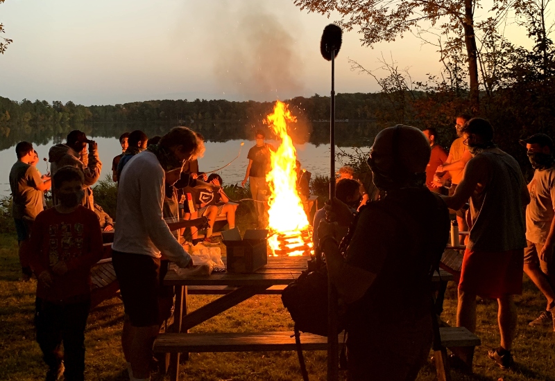 A group of North Star Camp campers and staff gather around a fire for s'mores while a NBC News crew films them for a newstory.