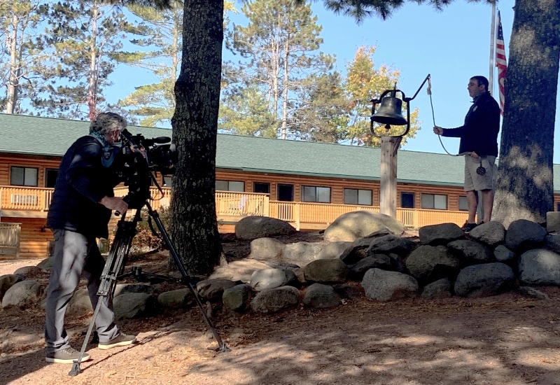 A NBC News cameraman films a North Star Camp director ringing the camp bell for a segment that aired on NBC Nightly News.