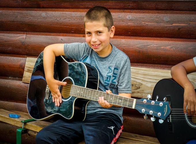 A camper at North Star Camp smiles as he learns how to play guitar.