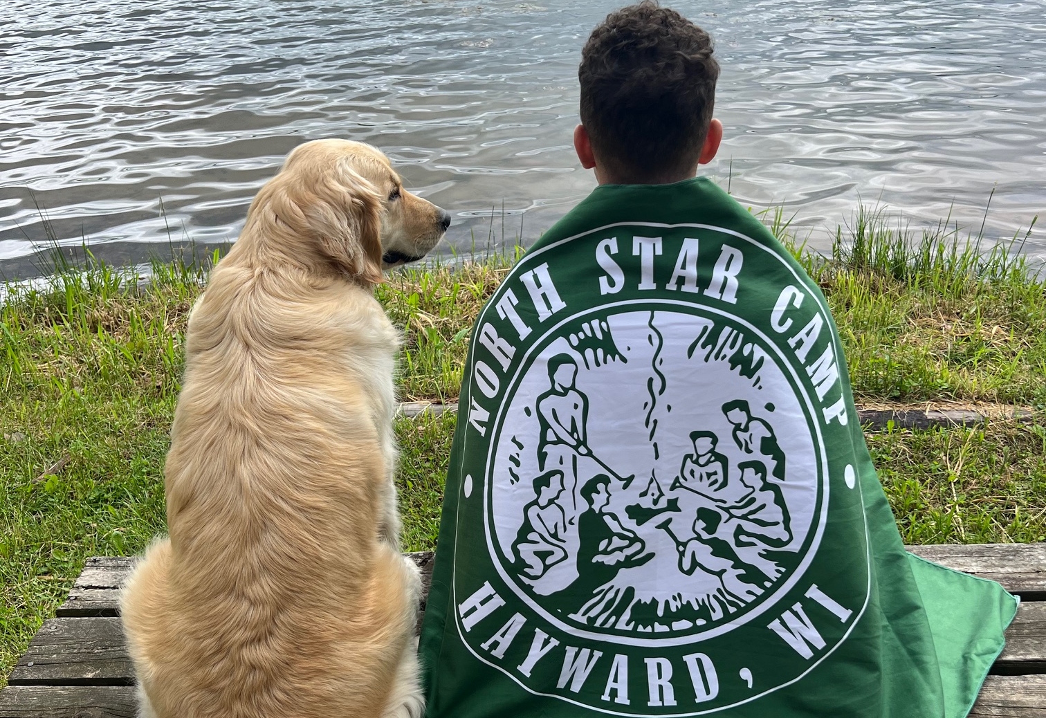 A dog and a counselor overlook Spider Lake as the counselor is wrapped in a North Star Camp towel.