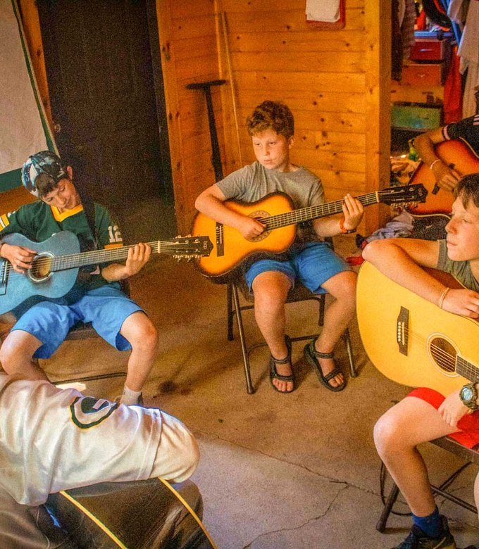 Campers play acoustic guitars together in the music room.