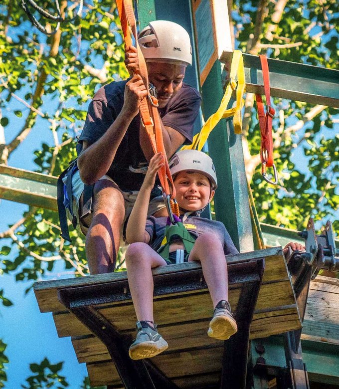 A counselor and camper sit on the high ropes course platform.