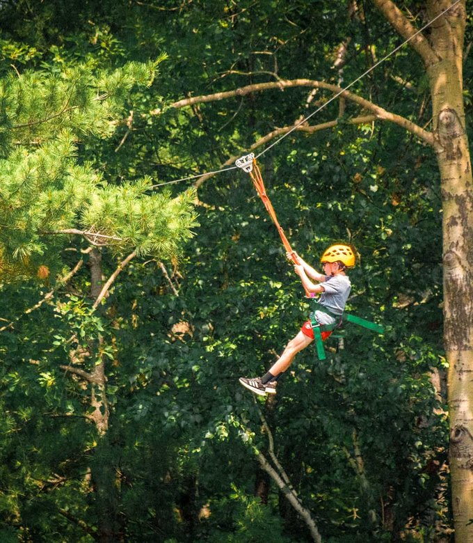 A camper rides the zip line through the trees.