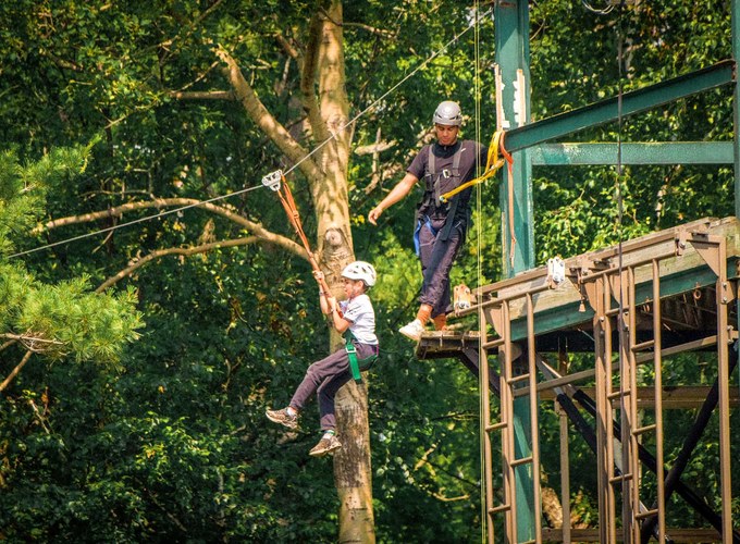 A camper crosses a high ropes element while a counselor spots from the platform above.