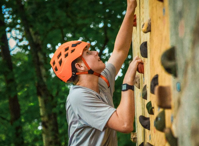 A camper in a helmet works his way up the rock climbing wall.