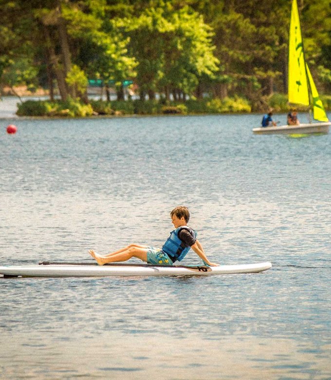 A camper sits on a stand up paddle board on Spider Lake.