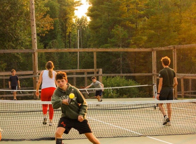 A camper serves during a tennis match on the camp courts.