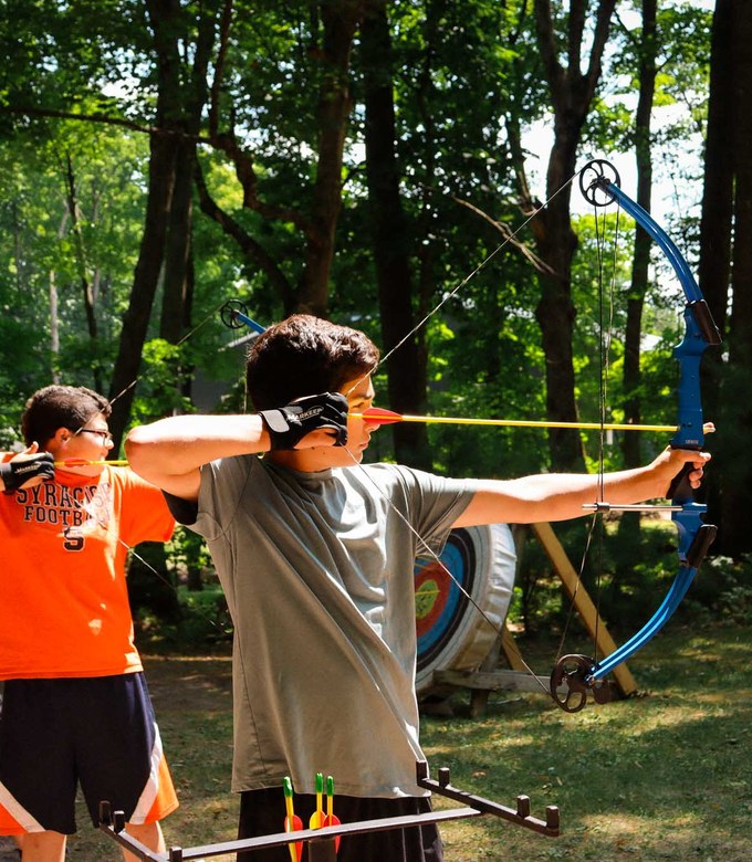 Two campers draw their bows side by side at the archery range.