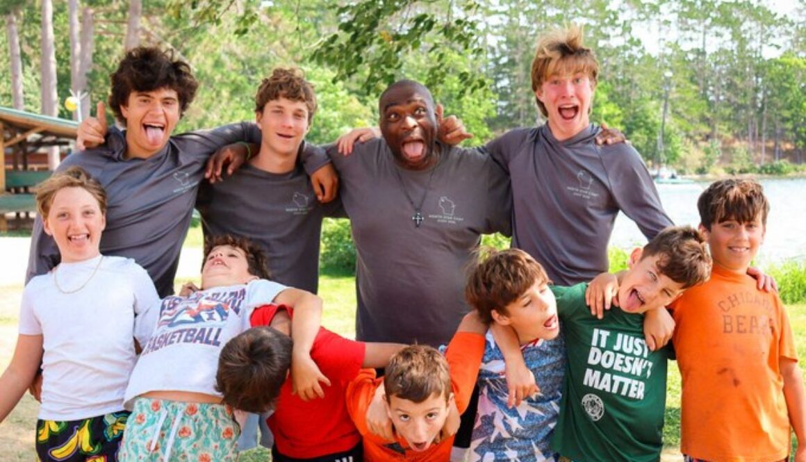Campers and their counselors stand arm in arm outside the cabins.
