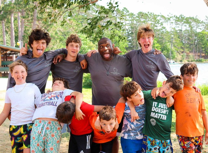 Campers and their counselors stand arm in arm outside the cabins.